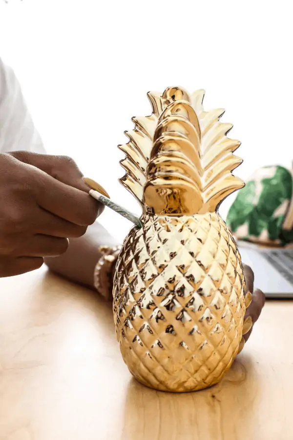 woman inserting money into a pineapple shaped money bank to save money